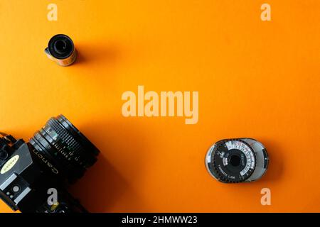 Lublin, Polen, 01. Februar 2022. Klassische Canon A1-Filmkamera, eine Rolle von Schwarz-Weiß-Film und analogem sekonic-Lichtmeter auf orangefarbenem Hintergrund - t Stockfoto