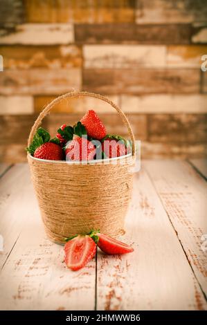 Obstkorb ist eine großartige Lösung für den Innenraum. Das Foto wurde gegen eine Backsteinmauer und auf einem Holztisch aufgenommen. Das Bild ist in warmen Farben gehalten Stockfoto