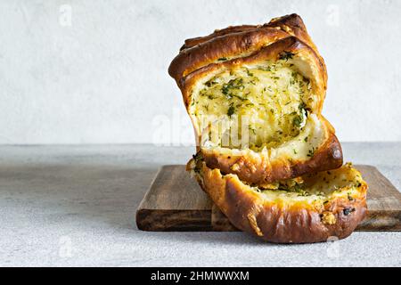 Hausgemachtes frisches Pull-Apart-Brot mit Kräutern (Petersilie, Thymian, Rosmarin, Dill), Knoblauch, Käse und würzige Butter auf einem Holzbrett. Stockfoto