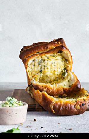 Hausgemachtes frisches Pull-Apart-Brot mit Kräutern (Petersilie, Thymian, Rosmarin, Dill), Knoblauch, Käse und würzige Butter auf einem Holzbrett. Stockfoto