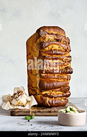 Hausgemachtes frisches Pull-Apart-Brot mit Kräutern (Petersilie, Thymian, Rosmarin, Dill), Knoblauch, Käse und würzige Butter auf einem Holzbrett. Stockfoto