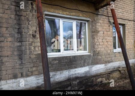 Gornyak, Ukraine. 9th. Februar 2022. Drei der Mazur-Kinder blicken am 9. Februar 2022 aus ihrem Wohnungsfenster.9. Februar 2022. Igor und Eugenia Mazur, die Eltern von 5 Kindern, die alle unter 8 Jahre alt sind, leben etwa 10 Meilen von der Donezker Front in Gornyak, Ukraine. Die Familie kämpft darum, genügend Arbeit für Lebensmittel und Rechnungen zu finden und bleibt besorgt, während die russischen Streitkräfte an der ukrainischen Grenze mobilisieren. (Bild: © Michaal Nigro/Pacific Press via ZUMA Press Wire) Stockfoto