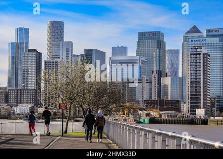 London, Großbritannien. 12th. Februar 2022. An einem herrlich sonnigen Tag in London laufen und joggen die Menschen entlang der Themse auf der Greenwich Peninsula mit Canary Wharf im Hintergrund. Kredit: Imageplotter/Alamy Live Nachrichten Stockfoto