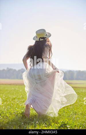 Junge schöne lange schwarze Haare asiatische Frau trägt ein lila romantisches Kleid stehen in einem hinterleuchteten Grasfeld Stockfoto