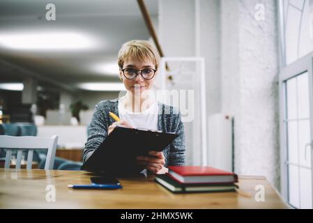 Lächelnde Frau, die während der Arbeit Bericht schreibt Stockfoto