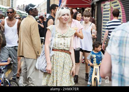 London, Großbritannien - am 17. Juli 2020 Spaziert Ein lächelndes Mädchen in einem blühenden Kleid an einem Sonntagnachmittag auf dem Columbia Flower Market durch die Menge Stockfoto