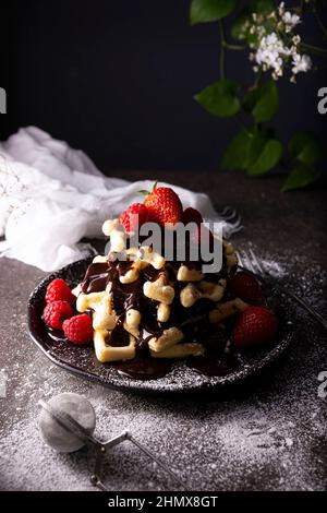 Darkfood-Stil Fotografie von hausgemachten Waffeln mit Schokolade, Früchten und Puderzucker Stockfoto