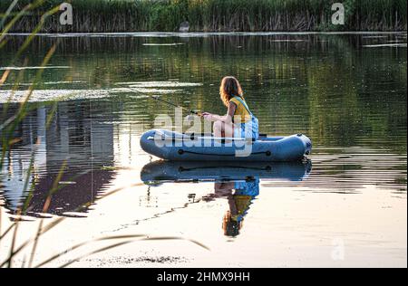 Mädchen auf dem Boot angeln. Angeln Kajak. Schöne Frau segelt auf einem aufblasbaren Boot mit einer Angelrute auf einem Sommersee. Stockfoto