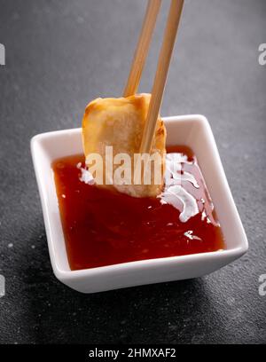 Frittierte knusprige Gyoza, die in süßer Chilisauce getaucht wird. Asiatische Küche. Stockfoto