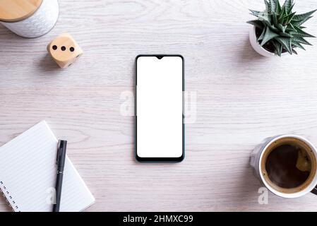 Flat Lay Phone Mockup Komposition auf Schreibtisch. Isolierter Bildschirm für die App-Präsentation. Pad mit Stift, Kaffeebecher, Pflanze und Box daneben. Sauberes Büro des Stockfoto