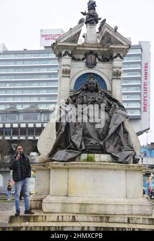 Ein Solo-Protestler fordert Freiheit und Gerechtigkeit für den Sudan, offiziell die Republik Sudan, ein Land im Nordosten Afrikas, neben der übergroßen Bronzestatue der Königin Victoria in Piccadilly Gardens, Manchester, England, Vereinigtes Königreich. Die Bronzestatue der Königin Victoria sitzt auf einem großen Thron und trägt ein Spitzenkleid mit dem Orden des Gewantes. Sie hält ein Zepter in der rechten Hand und einen Reichsapfel in der linken. Vor kurzem gingen im Sudan Tausende auf die Straßen des ganzen Landes und forderten zivile Herrschaft und Gerechtigkeit für die seit dem Putsch vom 25. Oktober Getöteten. Stockfoto