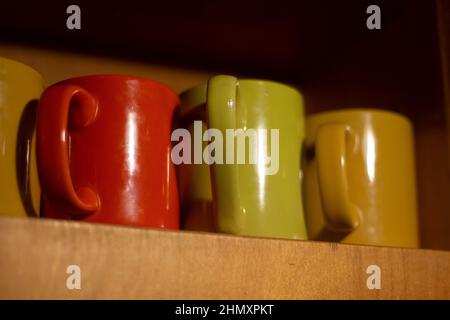 Tassen auf dem Regal. Bunte Gläser für Getränke. Utensilien in der Küche. Behälter für Flüssigkeiten. Details zur Innenausstattung. Teeset. Stockfoto