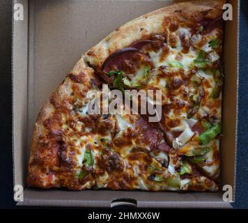 Zwei Scheiben Pepperoni-Pizza mit Tomatensauce, Käse, grünem Pfeffer und Pepperoni-Fleisch in einem Karton Stockfoto