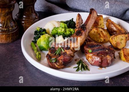 Nahaufnahme von Lammkoteletts mit Seiten von gebratenen Kartoffeln und Gemüse. Stockfoto