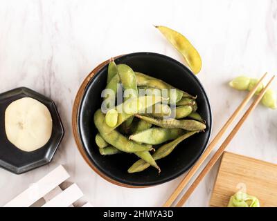 Gedämpfter Edamame in schwarzer Schale auf weißer Marmorplatte. Speicherplatz Kopieren Stockfoto