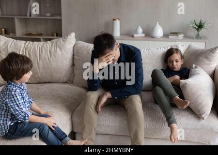 Müde Papa und gelangweilte Geschwister, die durch Konflikte gehen Stockfoto