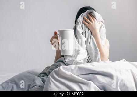 Eine Frau hält eine Tasse Kaffee, während sie im Bett liegt. Stockfoto