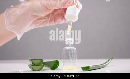 Spezialist tropft Aloe Saft in Glasflasche auf weißem Tisch Stockfoto