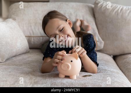 Glückliches Kind, das Geld sammelt und Münzen in ein Sparschwein fallen lässt Stockfoto