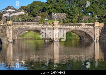 Der Blick auf die SeidenIshibashi-Brücke (ein Spitzname ist Meganebashi oder Brillen) über das Wasser des Nijubashi-Grabens und des Fushimi-Turms von Kyuden aus gesehen Stockfoto