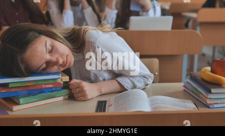 Ein müdes Schulmädchen schläft über ihren Lehrbüchern an ihrem Schreibtisch ein. Stockfoto