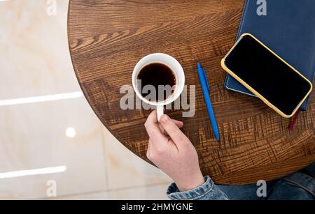 Eine Tasse Kaffee auf einem Holztisch und einem Notizblock, Draufsicht. Stockfoto