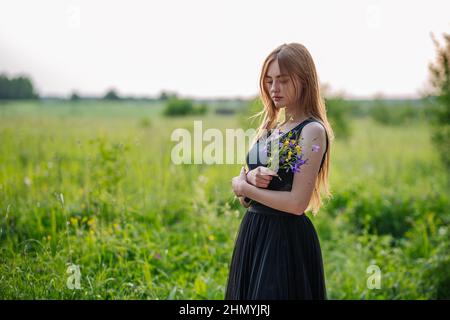 Porträt eines russischen Mädchens mit einem Strauß wilder Blumen am Abend im Dorf. Stockfoto