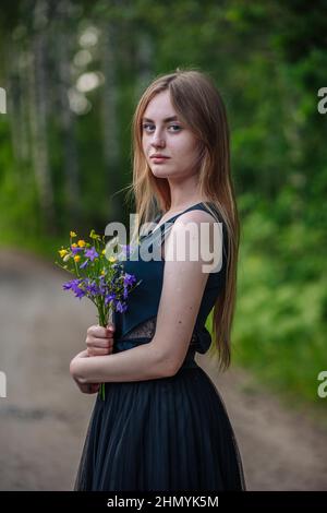 Porträt eines russischen Mädchens mit einem Strauß wilder Blumen am Abend im Dorf. Stockfoto