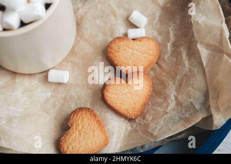 Cookies in Form von Herzen auf einem blauen Tablett, vor dem Hintergrund von Kaffee mit Marschmalchen. valentinstag-Konzept Stockfoto