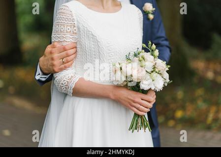 Ein zartes Brautstrauß in den Händen der Braut, die vom Bräutigam umarmt wird Stockfoto