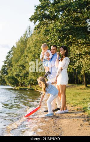 Eine glückliche Familie mit zwei Kindern hat Spaß im Sommer am See. Meine Tochter lässt ein Boot ins Wasser Stockfoto