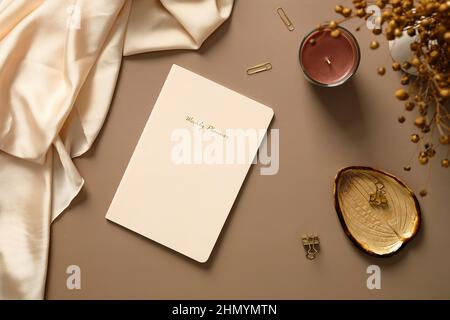 Wochenplaner Notizbuch, Kerze, Bürobedarf, Seide, getrocknete Blumen auf braunem Tisch. Femininer Arbeitsplatz, Schreibtisch für das Home Office. Stockfoto