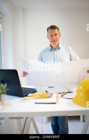 Architekt mit blauem Hemd steht am höhenverstellbaren Arbeitstisch und arbeitet Stockfoto