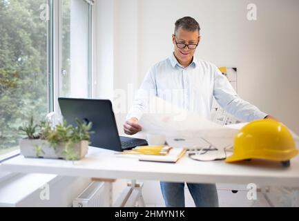 Architekt mit blauem Hemd steht am höhenverstellbaren Arbeitstisch und arbeitet Stockfoto