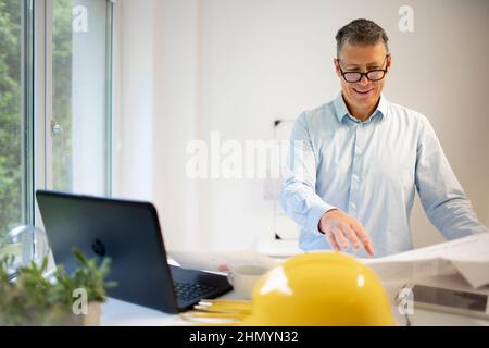 Architekt mit blauem Hemd steht am höhenverstellbaren Arbeitstisch und arbeitet Stockfoto