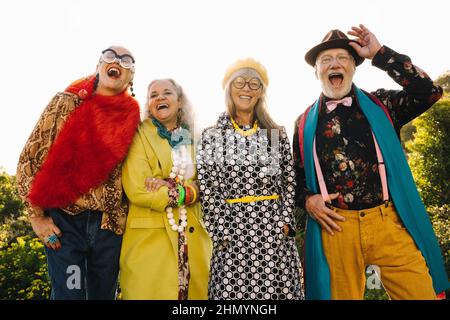 Gruppe exzentrischer reifer Freunde, die fröhlich lachen, während sie zusammen in einem Park stehen. Stilvolle ältere Menschen in farbenfroher Freizeitkleidung. Carefr Stockfoto