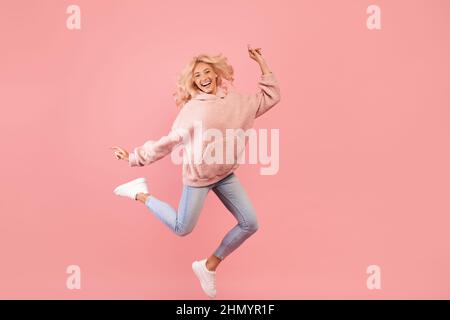 Spaß haben. Ganzkörperportrait mit einer verspielten Dame, die springt, tanzt und lächelt, während sie gut gelaunt ist Stockfoto