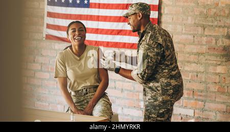 Glückliche Militärangehörende, die im Militärkrankenhaus eine Dosis des Covid-19-Impfstoffs erhalten hat. Amerikanische Soldatin lacht glücklich, während sie sich injiziert Stockfoto