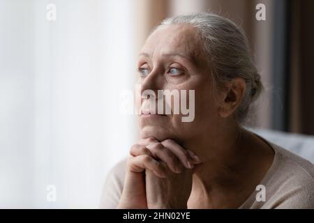 Nachdenklich gelangweilte ältere 70s-Mann-Frau, die auf das Fenster schaute Stockfoto