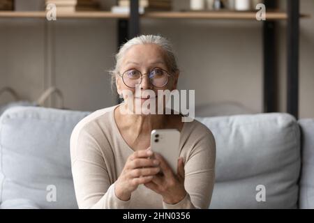 Fröhliche, fröhliche ältere Dame in einer Brille, die das Smartphone hält Stockfoto
