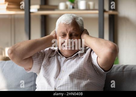 Glücklicher älterer Mann mit geschlossenen Augen, die die Ohren bedecken Stockfoto