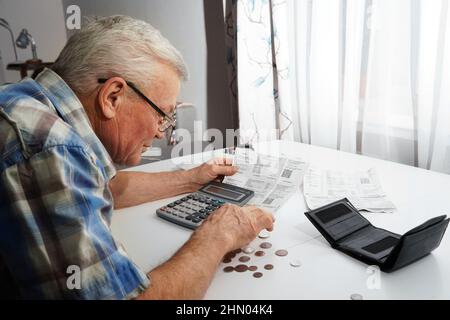 Verärgert Senior Mann am Tisch sitzen und Finanzen berechnen. Alter Mann, der Rechnungen überprüft. Mann, der Münzen auf dem Tisch zählt. Pensionsberechnungskonzept Stockfoto