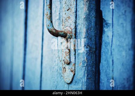 Eine alte blaue Holztür mit einem rostigen Metallgriff. Eine geschlossene Tür zum Haus. Das Geheimnis liegt hinter der Tür. Retro. Stockfoto