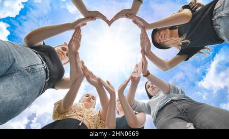 Freundinnen Mädchen machen eine Herzform aus ihren Händen vor dem Hintergrund eines fabelhaften Himmels. Stockfoto