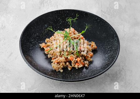 Zum Hauptgericht - Buchweizenbrei mit den Scheiben der gebratenen Karotte auf dem Teller garnieren Stockfoto