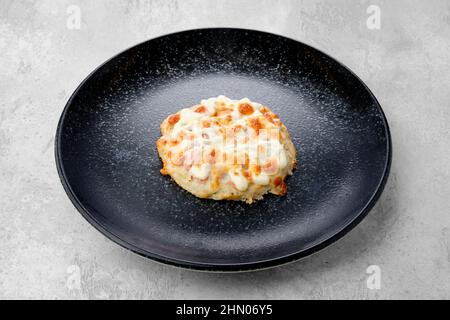 Gehacktes Schweinekotelett, das mit Schinken und Käse auf einem Teller gebacken wurde Stockfoto