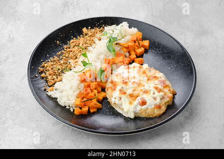 Gehacktes Schweinekotelett, gebacken mit Schinken und Käse, serviert mit Karotten und Reis auf einem Teller Stockfoto