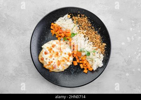 Gehacktes Schweinekotelett, gebacken mit Schinken und Käse, serviert mit Karotten und Reis auf einem Teller, Draufsicht Stockfoto