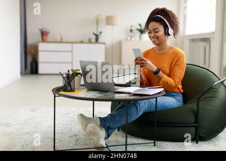 Lächelnde schwarze Frau mit schnurlosem Kopf und Mobiltelefon Stockfoto