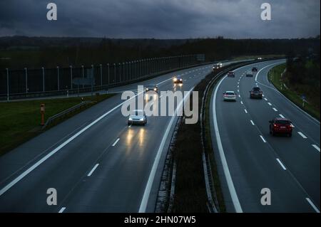 Fahren von Autos auf einer nassen Autobahn in der Dämmerung unter einem bewölkten Himmel in Deutschland, Bewegungsunschärfe, Kopierraum, ausgewählter Fokus, enge Schärfentiefe Stockfoto